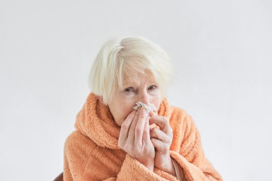 Senior woman blows her nose due to being sick