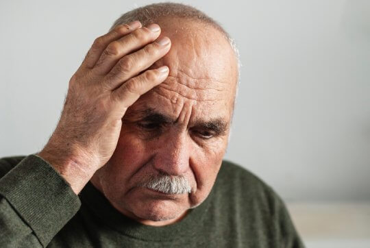 Forgetful senior man holding a hand to his head